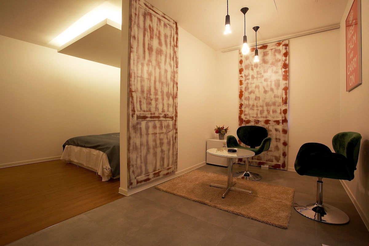 A small, well-lit bedroom with a bed, a desk, two chairs, and a rug.