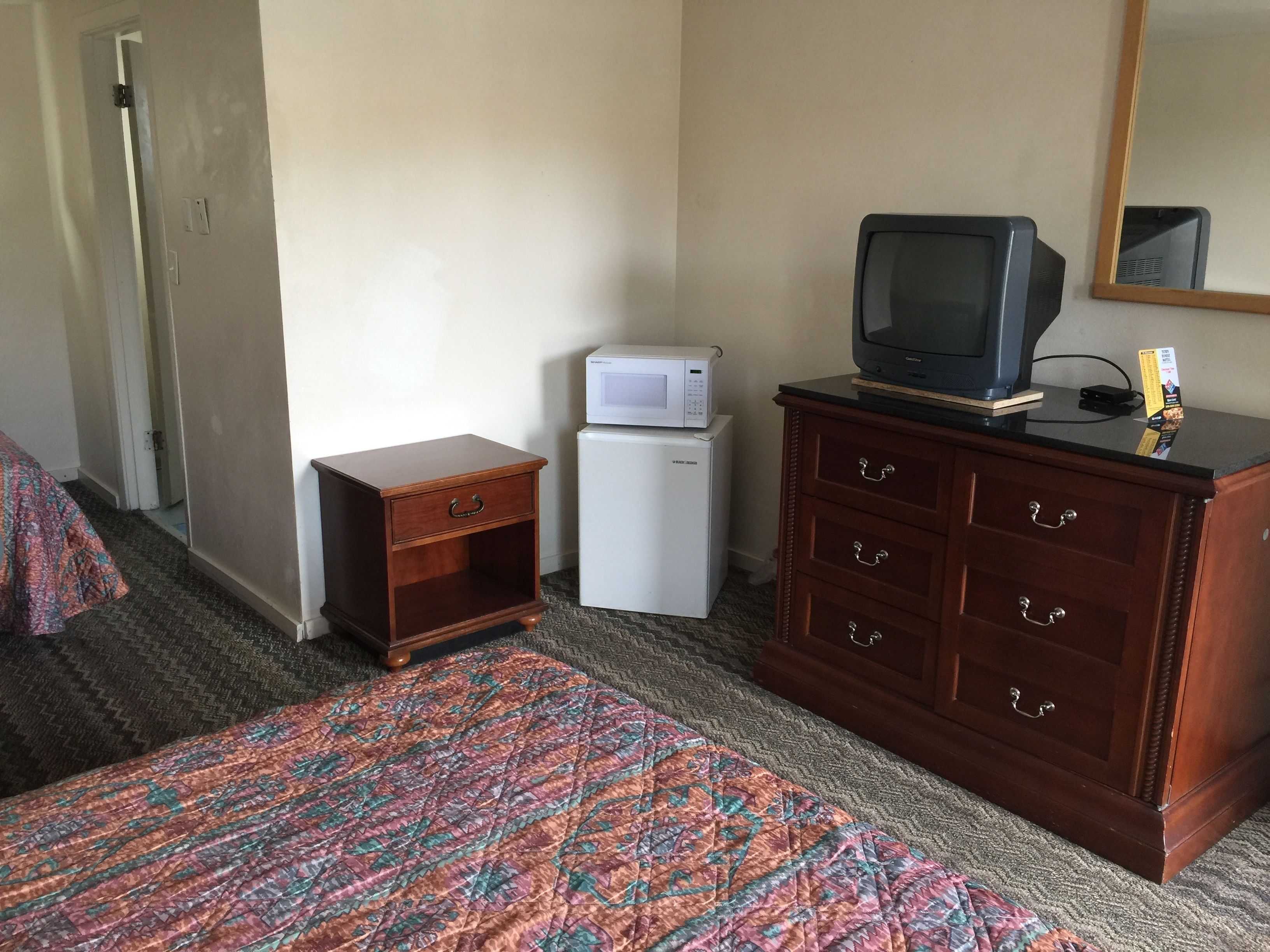 Une chambre d’hôtel équipée d’un lit, d’une commode en bois, d’une télévision, d’un four à micro-ondes et d’un réfrigérateur.