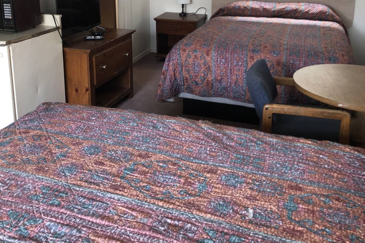 A hotel room with two beds, a desk with a computer, a small table, and a window with curtains.