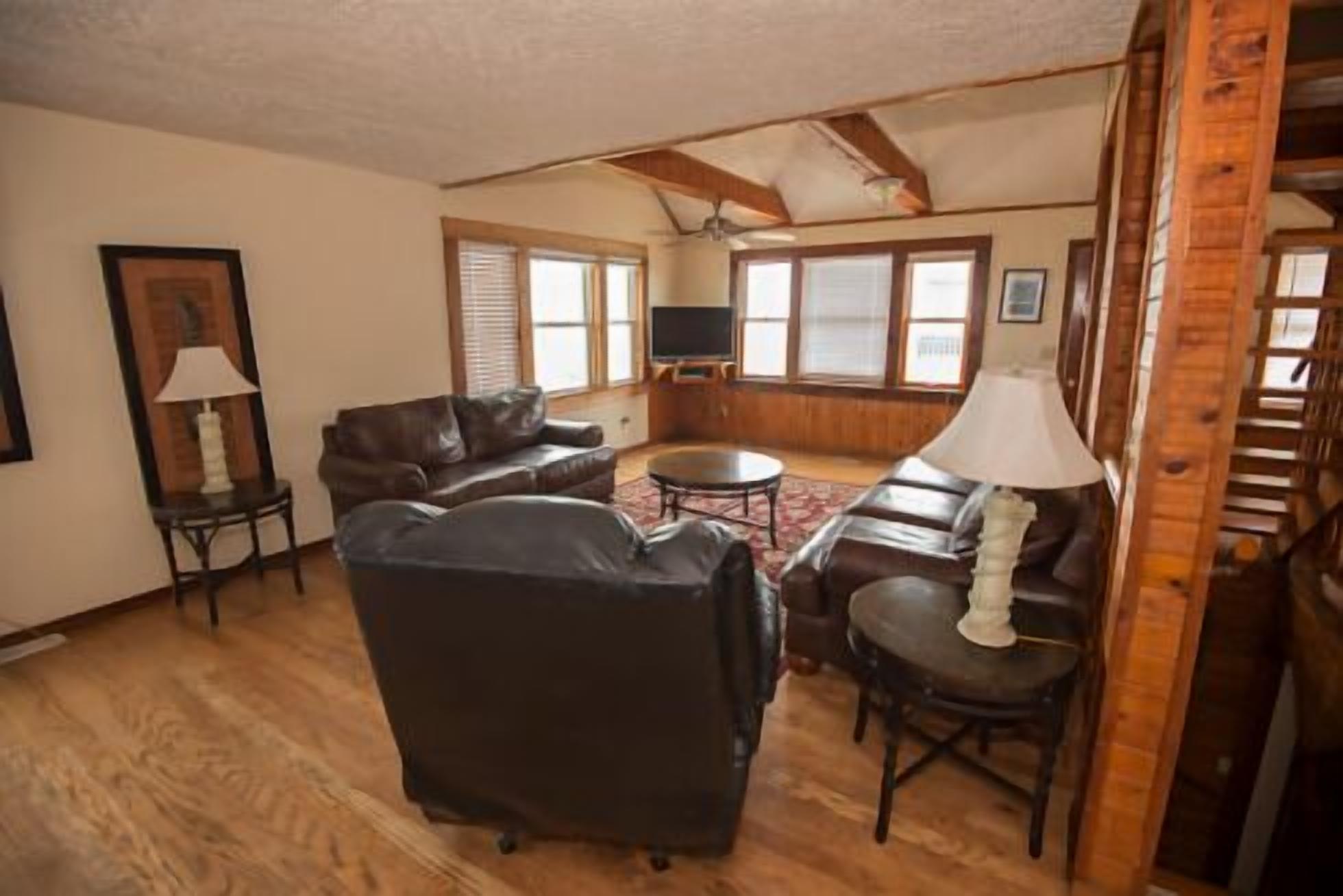 Una sala de estar con chimenea, sofás de cuero, televisor y piso de madera.