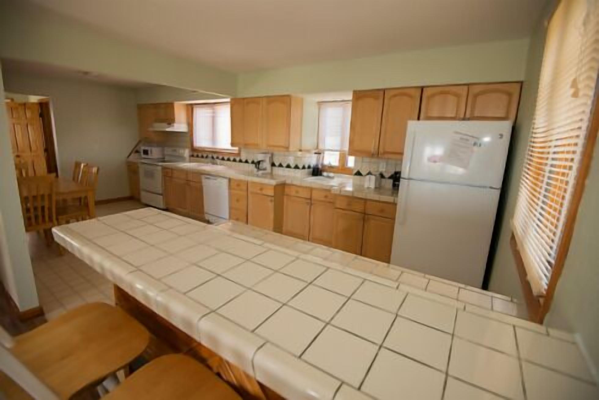 A kitchen with wooden cabinets, a tiled countertop, and a refrigerator.