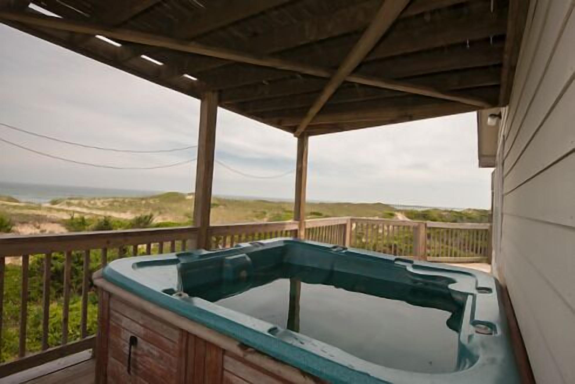 A hot tub on a wooden deck with a view of the beach and dunes.