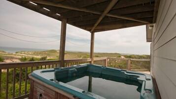 A hot tub on a wooden deck with a view of the beach and dunes.