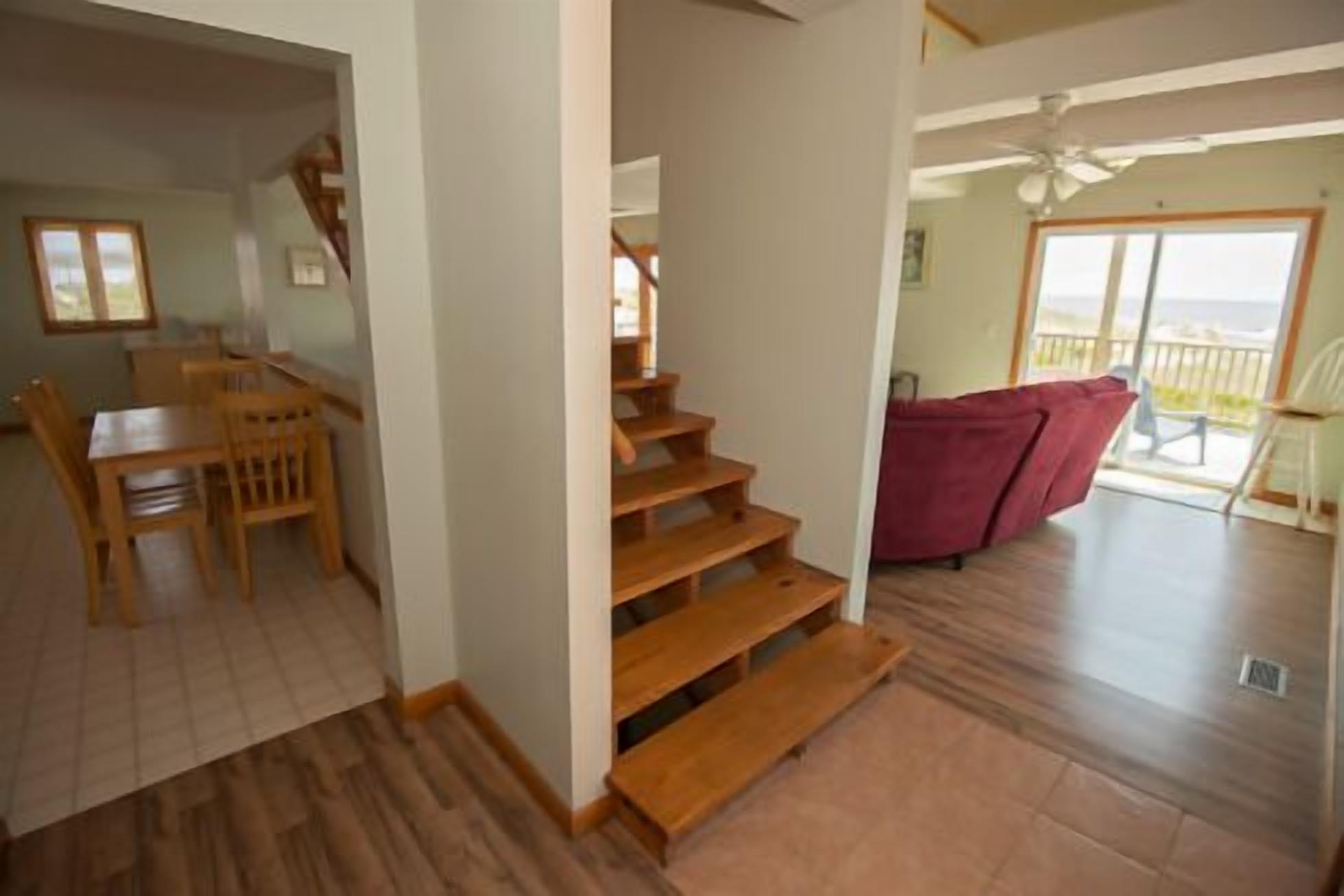 A staircase leading to a balcony with a red sofa, wooden flooring, and a dining area with chairs and a table.