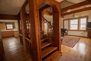 Un espacio habitable amplio con una escalera de madera, una cocina con armarios de madera y un ventanal que proporciona luz natural.