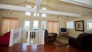 A spacious living room with a high ceiling, a white railing, a red sofa, a brown sofa, a television, and a framed picture on the wall. - Avon Cottages (Avon)