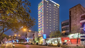 A multi-story hotel with illuminated signage, a modern facade, and a well-lit street in the foreground. - Lavender Riverside Hotel (Da Nang)