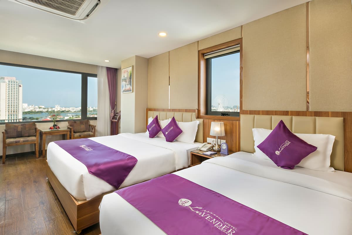 A hotel room with two beds, a desk, and a view of the city.