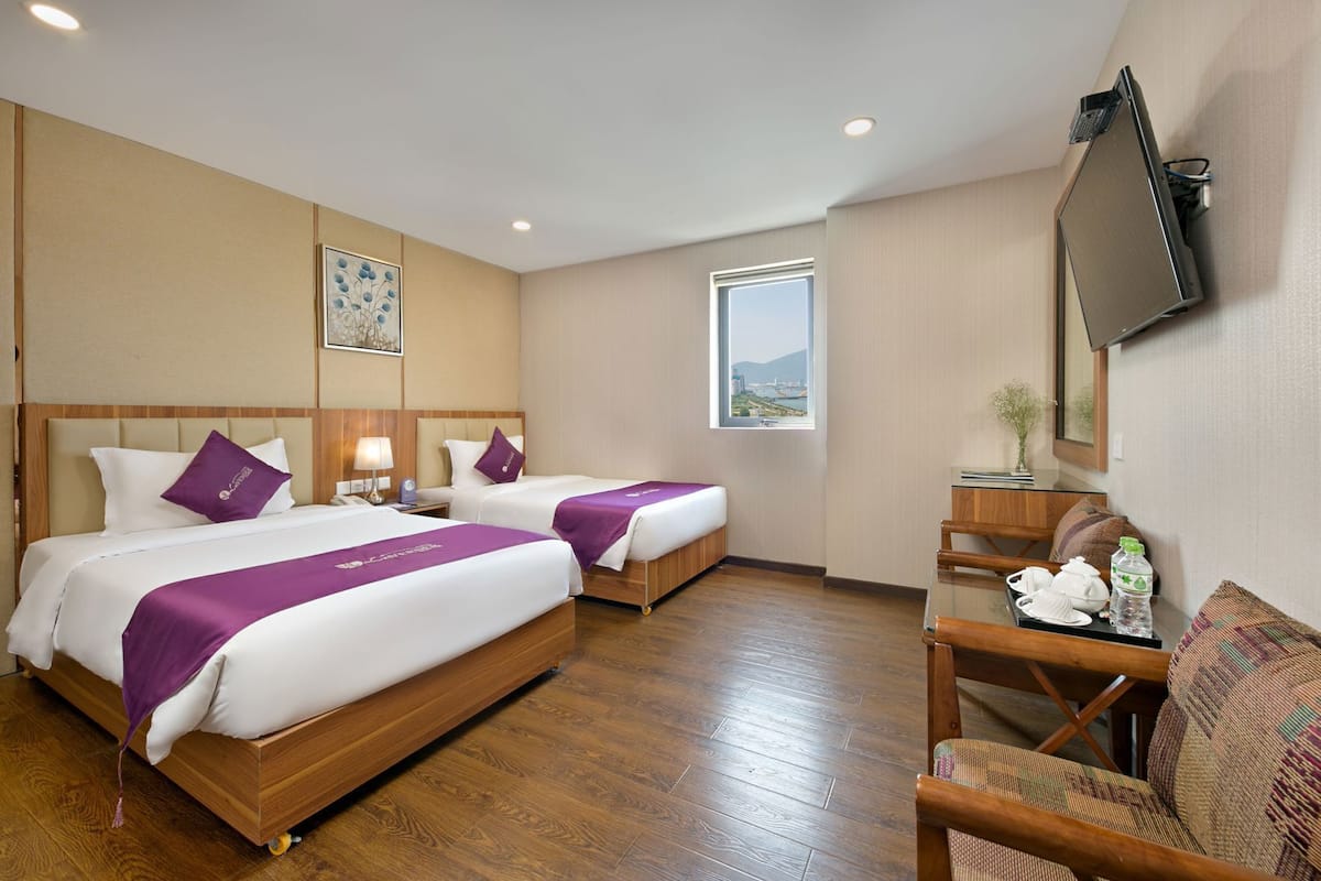 A hotel room with two beds, a desk, a chair, a TV, and a window with a view.