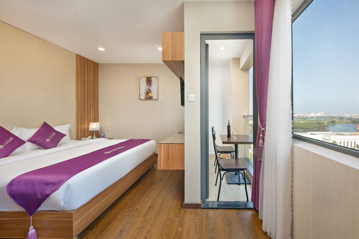 A hotel room with a large bed, a desk, and a view of the city through a window.