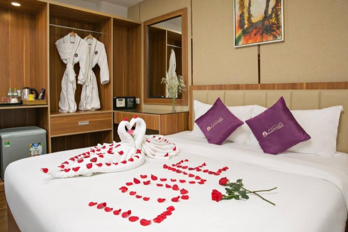 A hotel room with a bed, a robe rack, a mirror, and a painting on the wall.