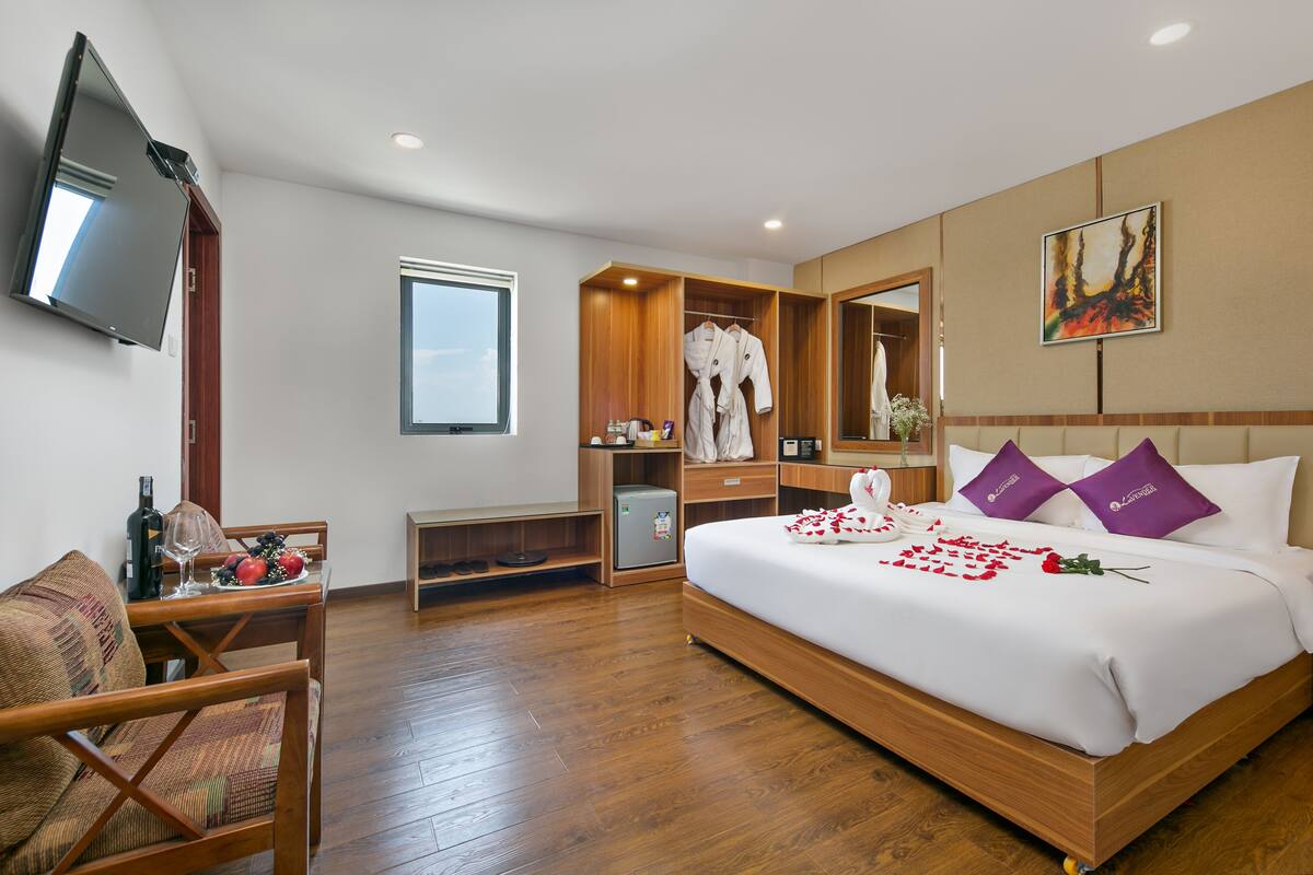 A hotel room with a large bed, a wooden wardrobe, a seating area with a sofa and table, and a television mounted on the wall.