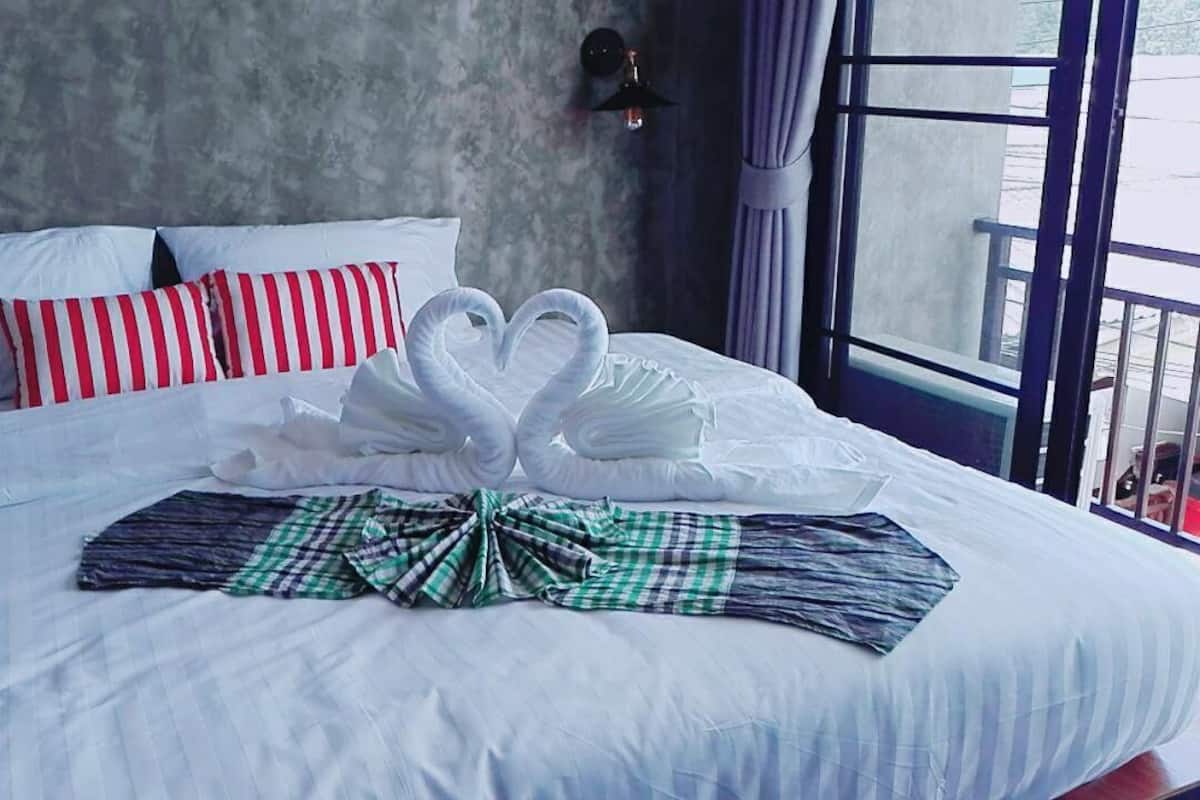 A neatly made bed with white linens, a red and white striped pillow, and a green and black checkered blanket.