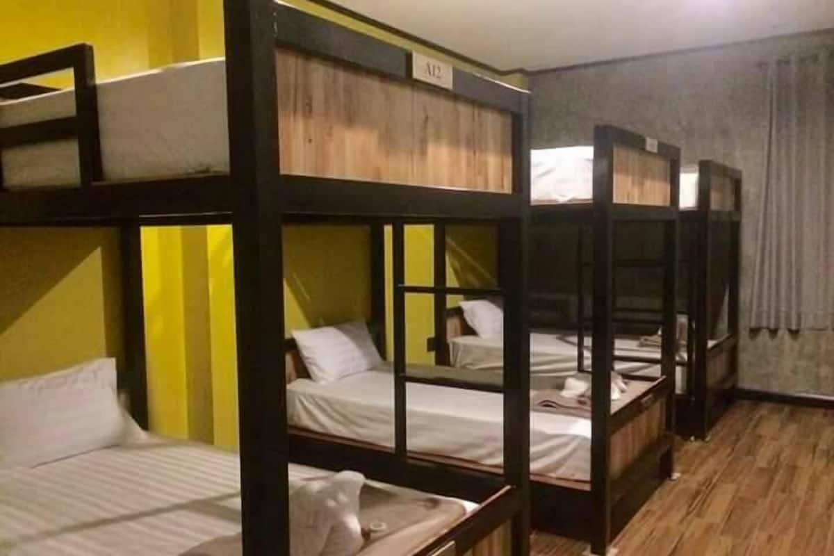 A room with bunk beds, wooden flooring, and a curtain on the window.