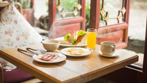 A breakfast tray with eggs, toast, and juice on a wooden table near a window with a view of greenery. - Ivy Garden Hotels & Resorts - Lijiang Henghehao (Lijiang)