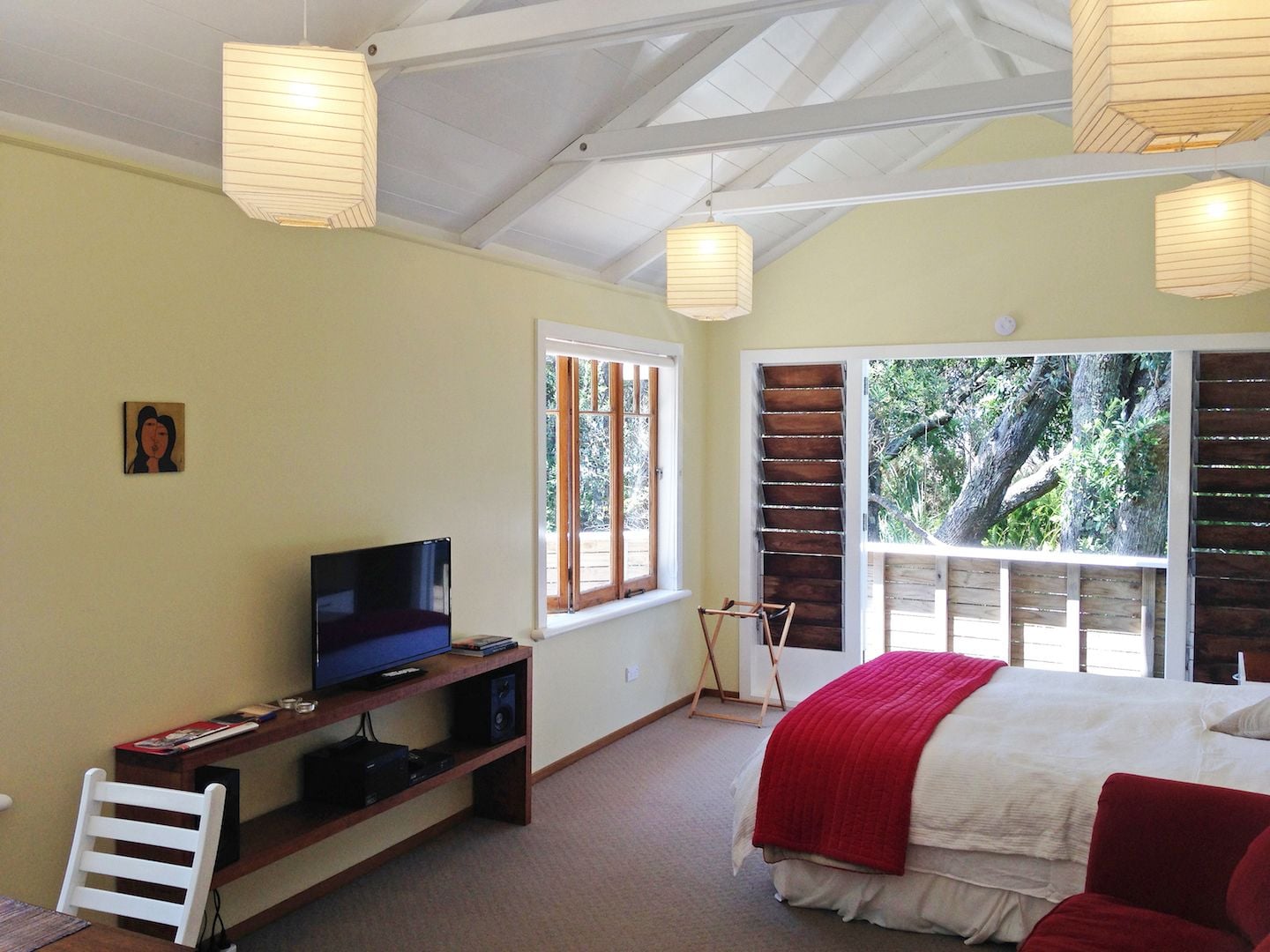 A bedroom with a bed, a TV on a stand, a window, and a door leading outside.