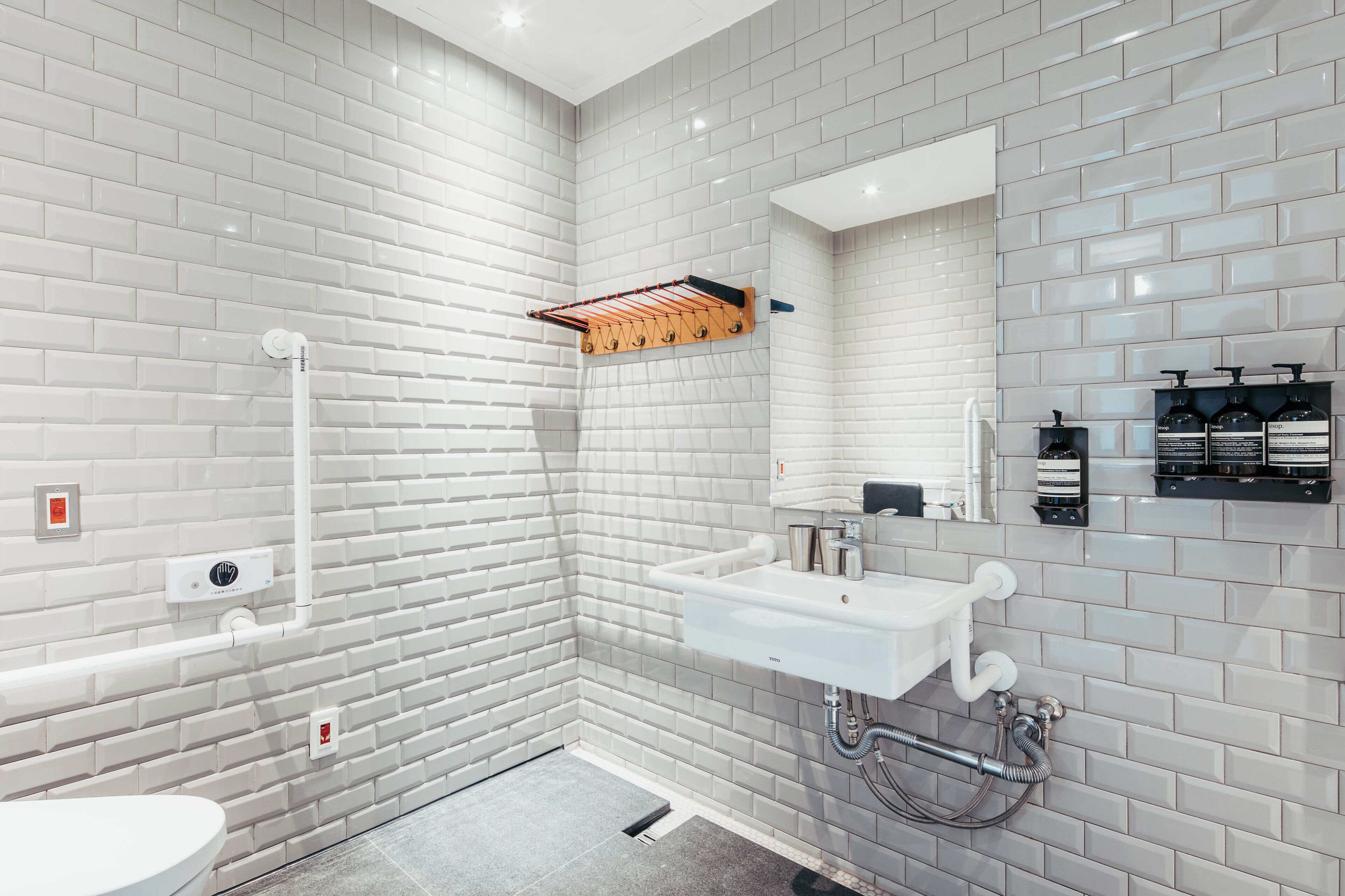 Un baño moderno con azulejos blancos tipo metro, un lavamanos blanco, un espejo, una ducha y un perchero para toallas.