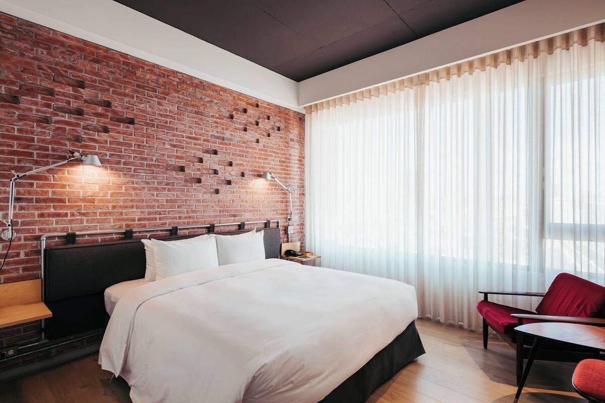 A hotel room with a brick wall, a large bed, a desk, and a chair.
