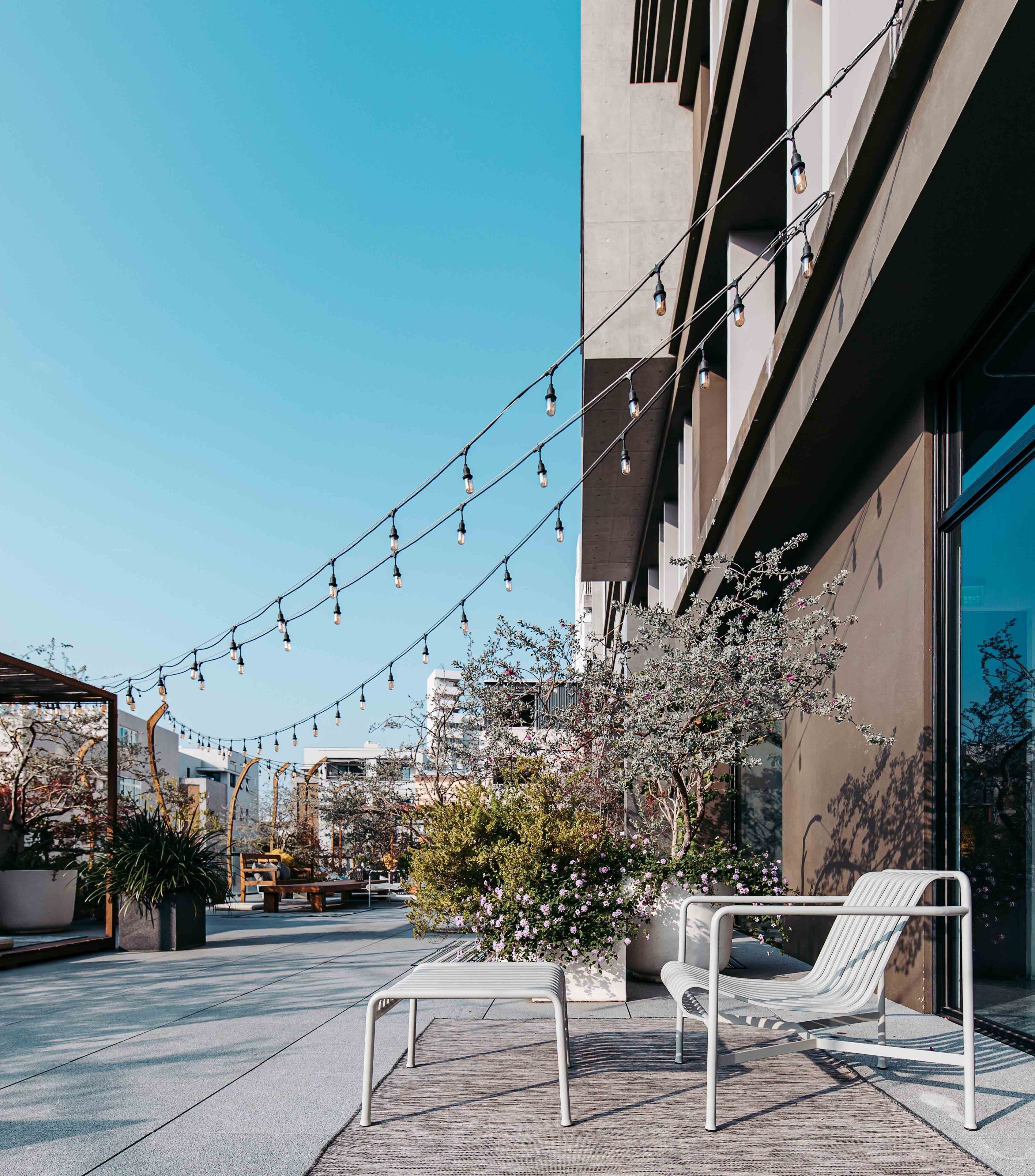 Un espace extérieur aménagé avec un banc et une table blancs, des guirlandes lumineuses et des plantes en pot.