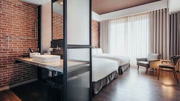 Habitación de hotel moderna con pared de ladrillo, una cama grande, un escritorio con lavamanos y una silla.