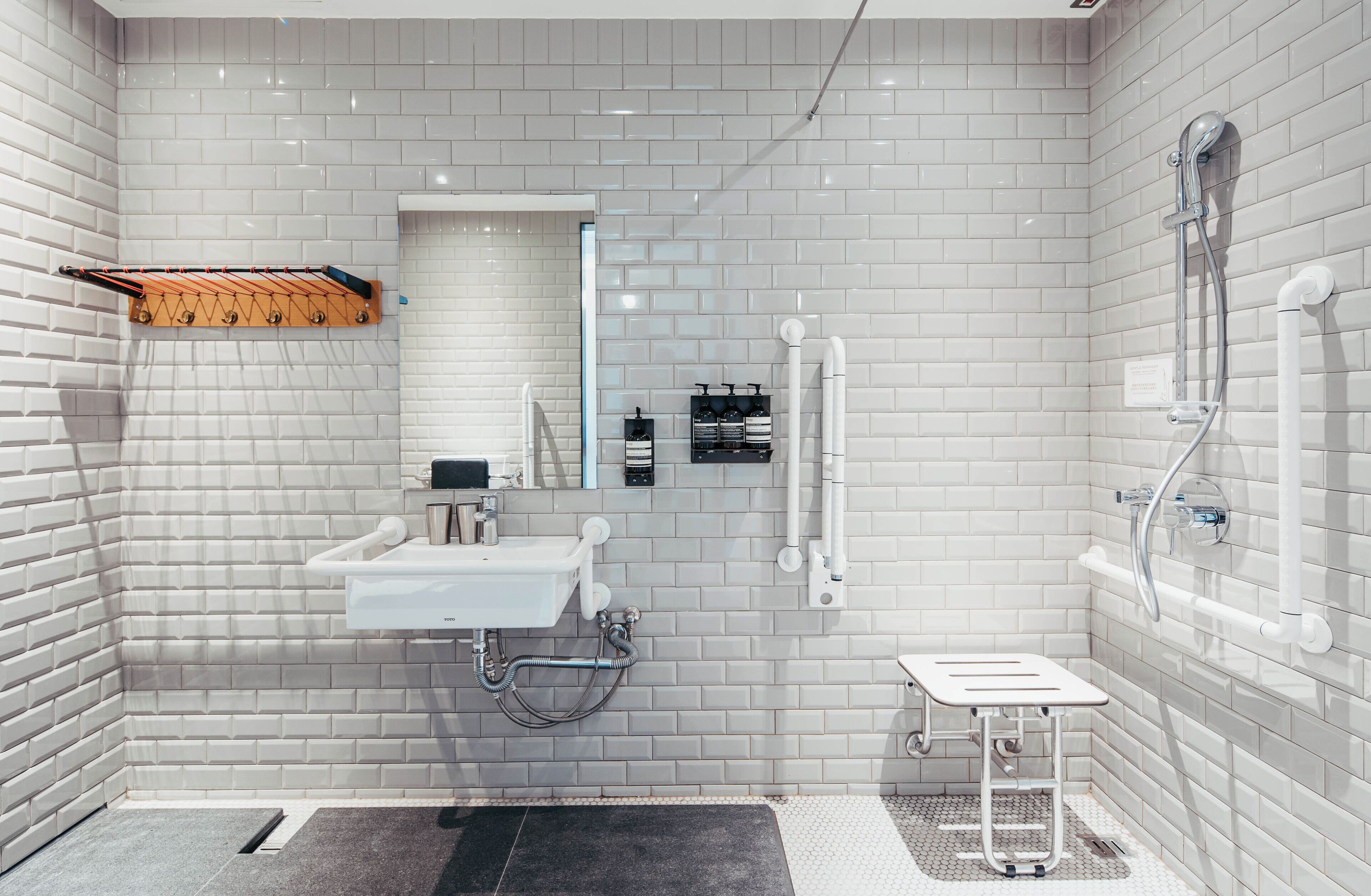 A modern bathroom with white tiled walls, a sink, a mirror, and a shower.