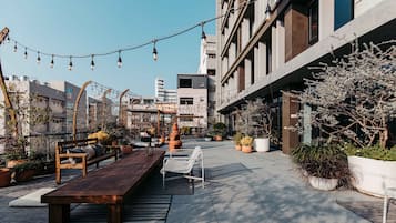 An outdoor seating area with a wooden bench and a white chair, surrounded by potted plants and string lights.