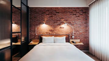 A hotel room with a brick wall, a bed with white linens, two bedside lamps, and a wooden nightstand with a phone.