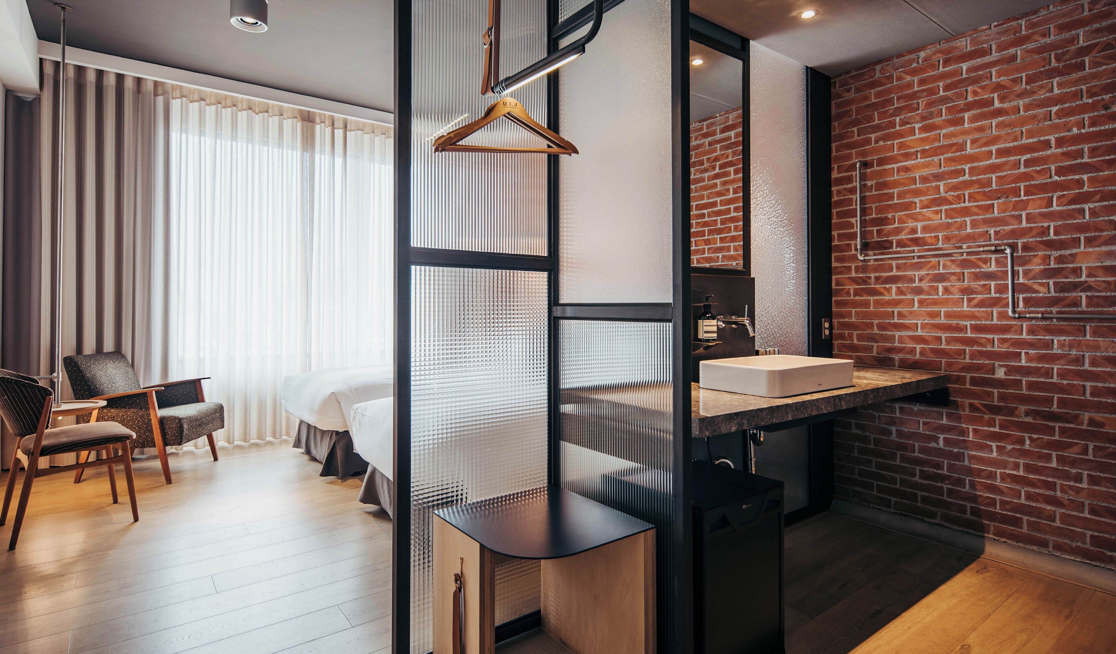 A modern hotel room with a bed, a desk, and a bathroom with a large mirror and a sink.