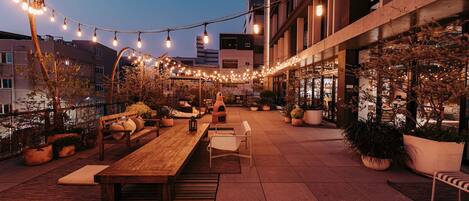 An outdoor patio area with a wooden table and chairs, surrounded by potted plants and string lights.