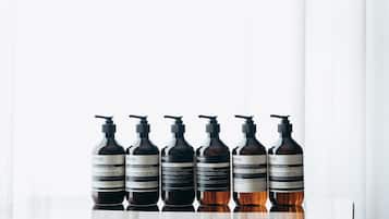 A row of six dark brown bottles with pump dispensers on a reflective surface.