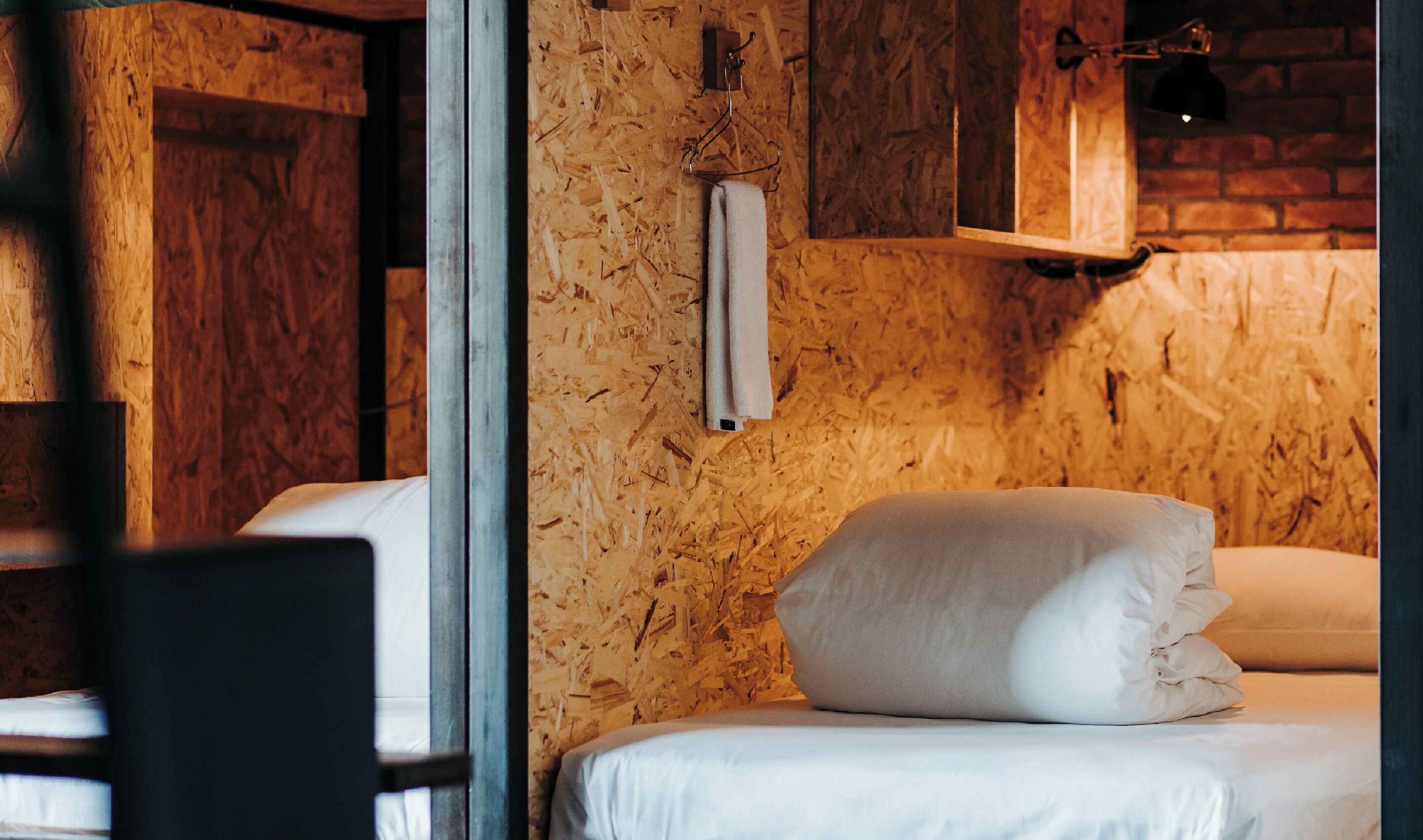 A room with a wooden wall, a hanging towel, and a bed with white bedding.