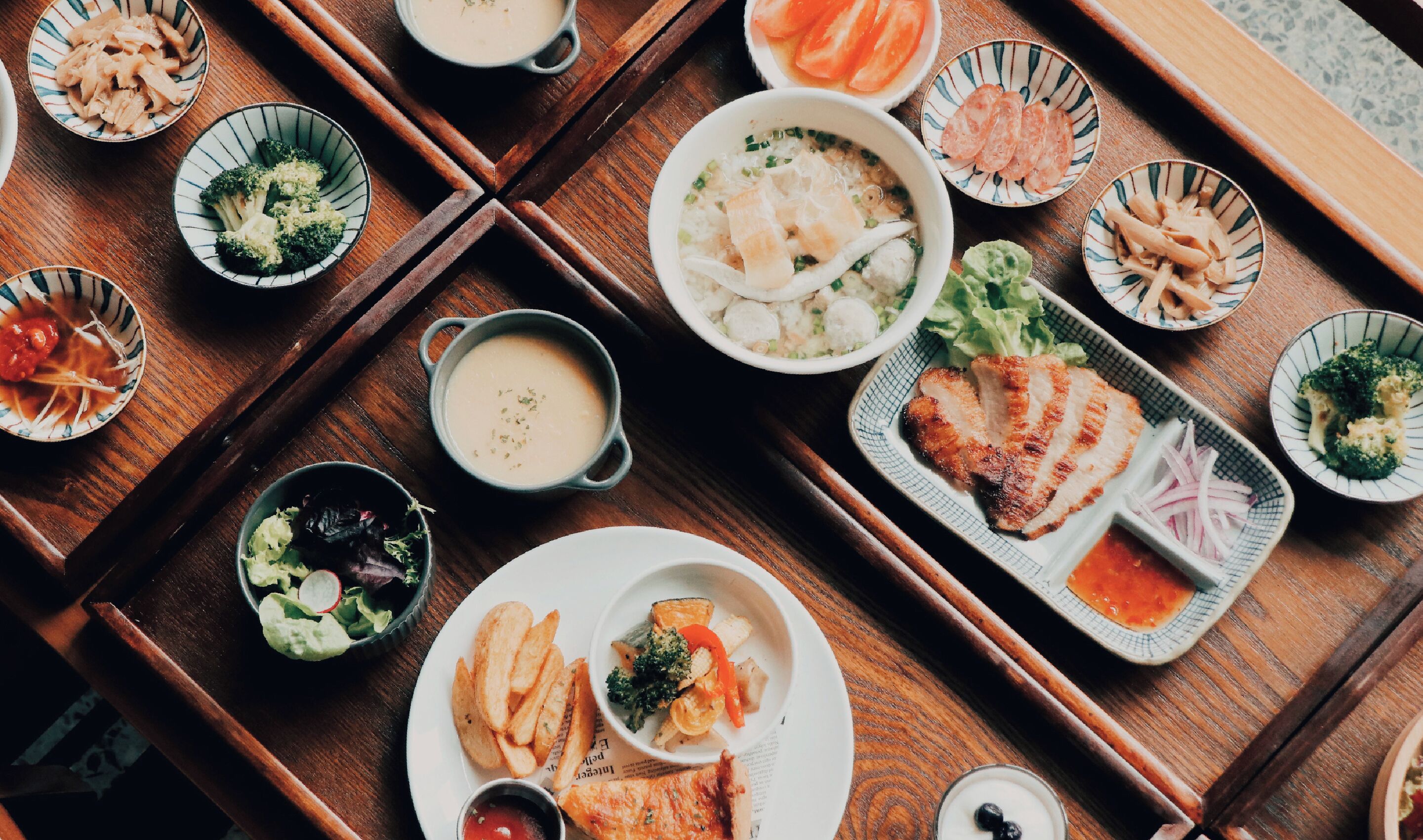 Een houten tafel met verschillende gerechten, waaronder sushi, sashimi en een kom soep.