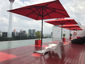 A rooftop terrace with red umbrellas, a white chair, and a view of the city skyline. - theRED (Kuala Lumpur)