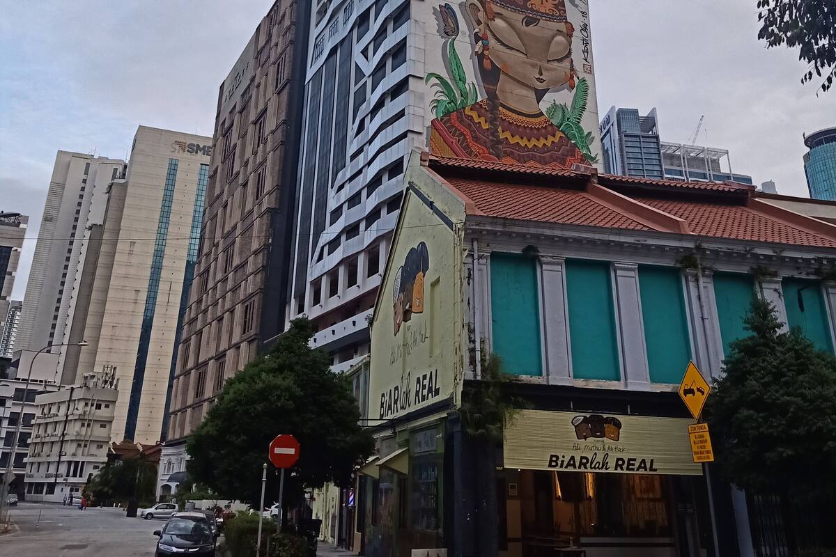 Un edificio alto con un mural colorido en su fachada, un letrero que dice 'Biarrah REAL', y una vista de la calle con coches y un paso de peatones.
