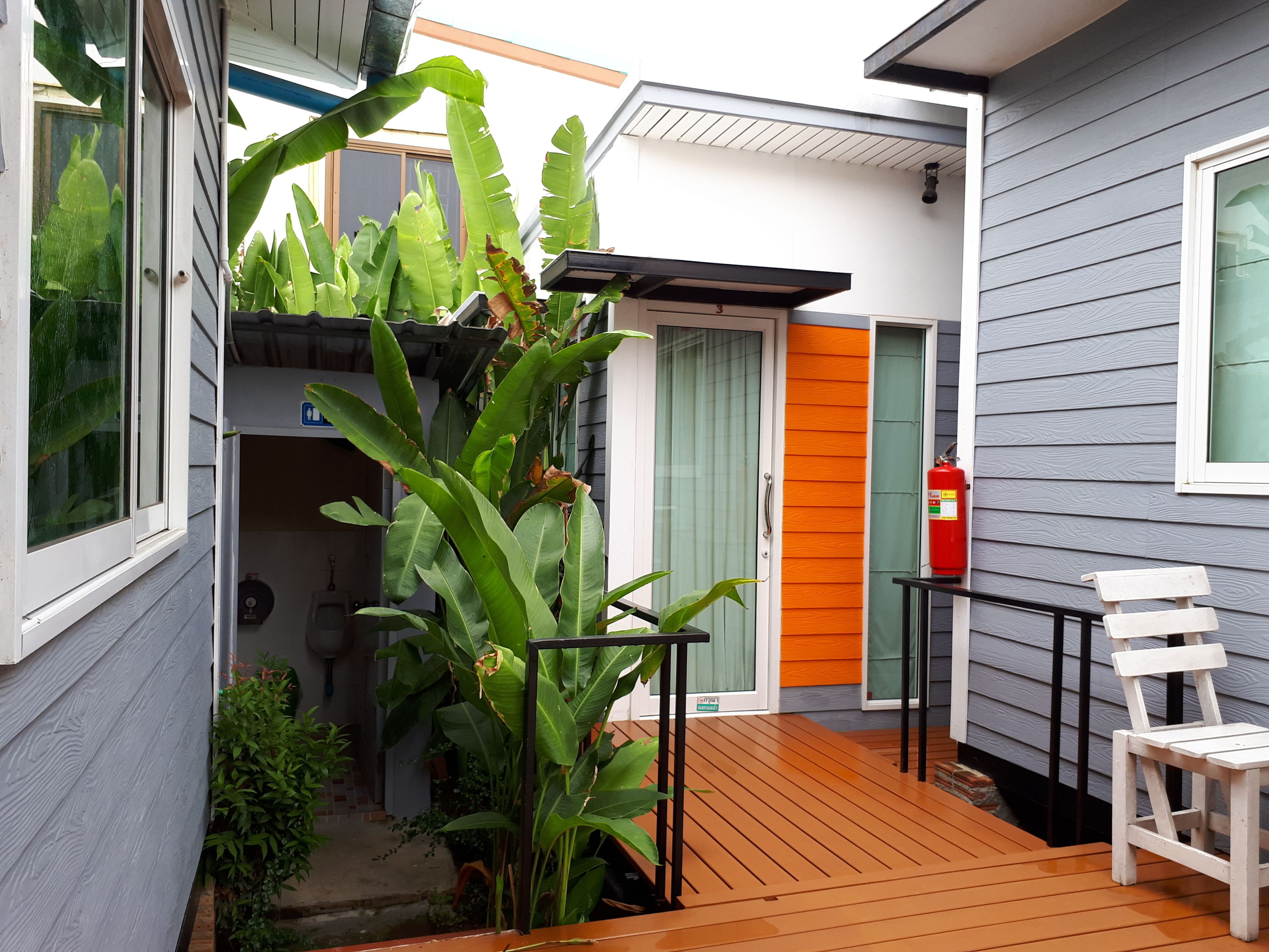 Una terraza de madera con una silla blanca, un extintor y una puerta con detalles en naranja.