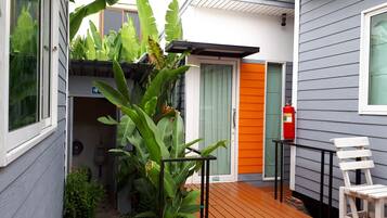 Una terraza de madera con una silla blanca, un extintor y una puerta con detalles en naranja.