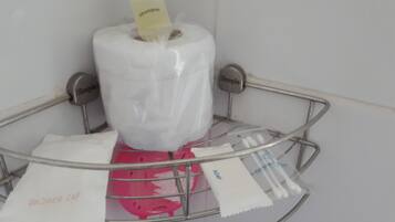 Ein Badezimmer mit einem Metall-Duschkorb, der eine Toilettenpapierrolle, eine Duschhaube und eine kleine Shampoo-Flasche enthält.