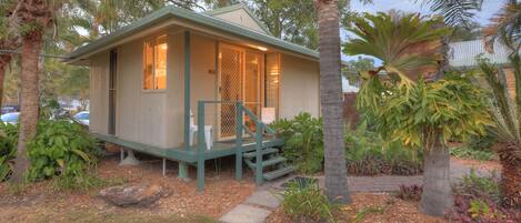 A small, single-story house with a porch, surrounded by tropical vegetation.