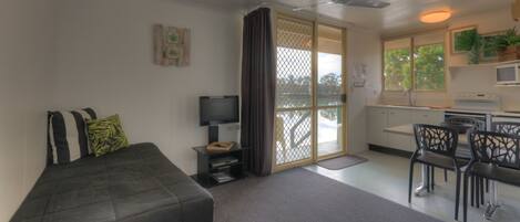 A compact room with a bed, a TV, a dining area, and a kitchen.