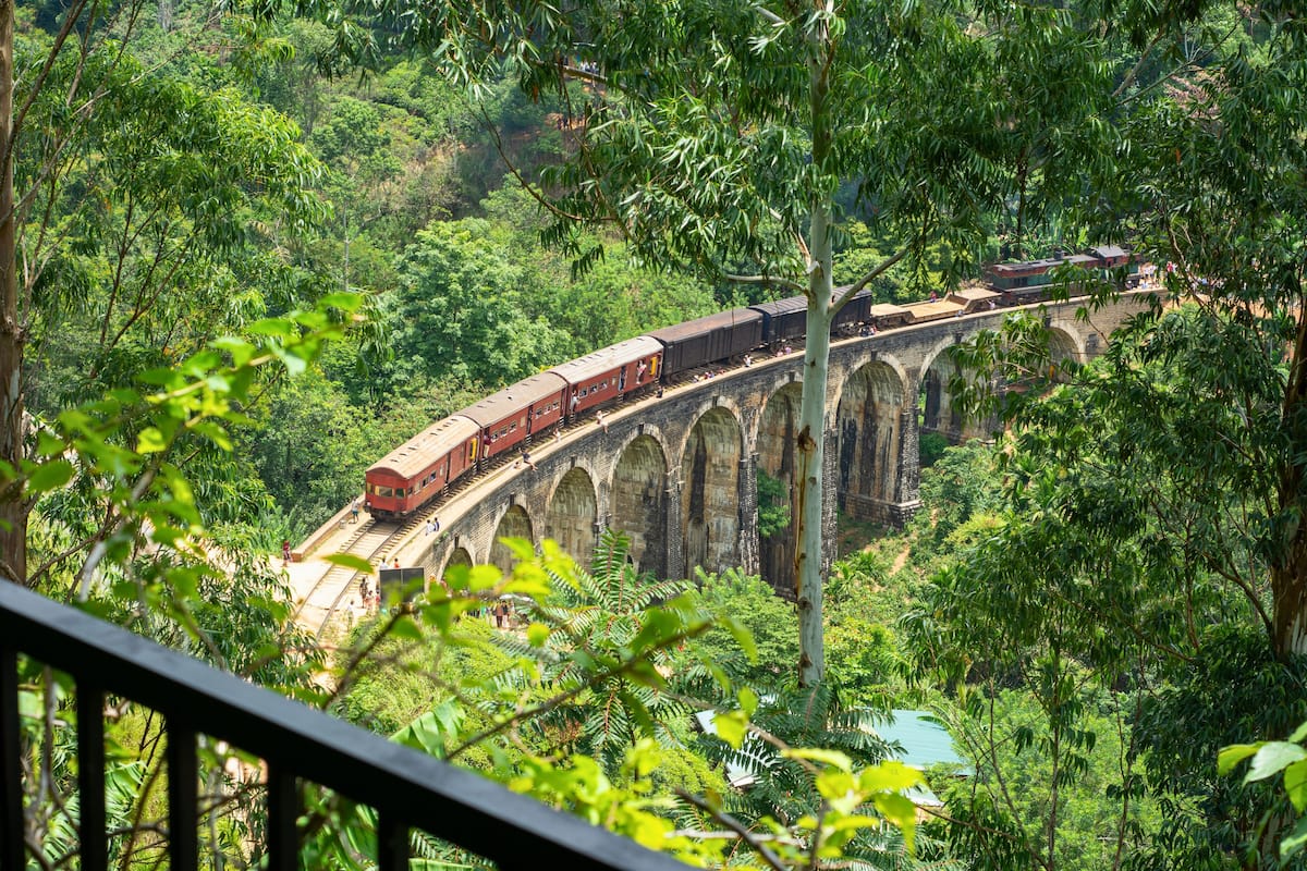 A train on an arched bridge surrounded by lush greenery.