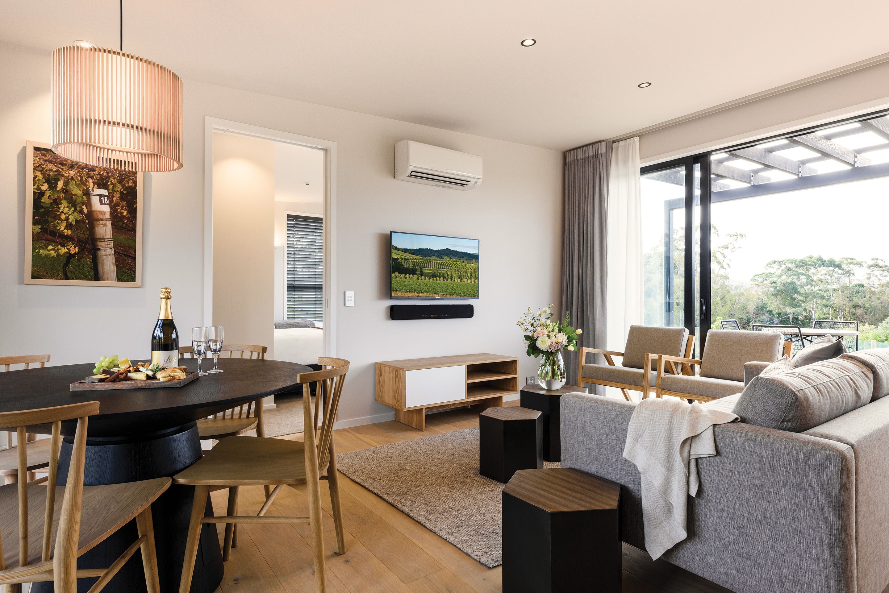 A modern living room with a dining area, a sofa, a TV, and a large window with a view.