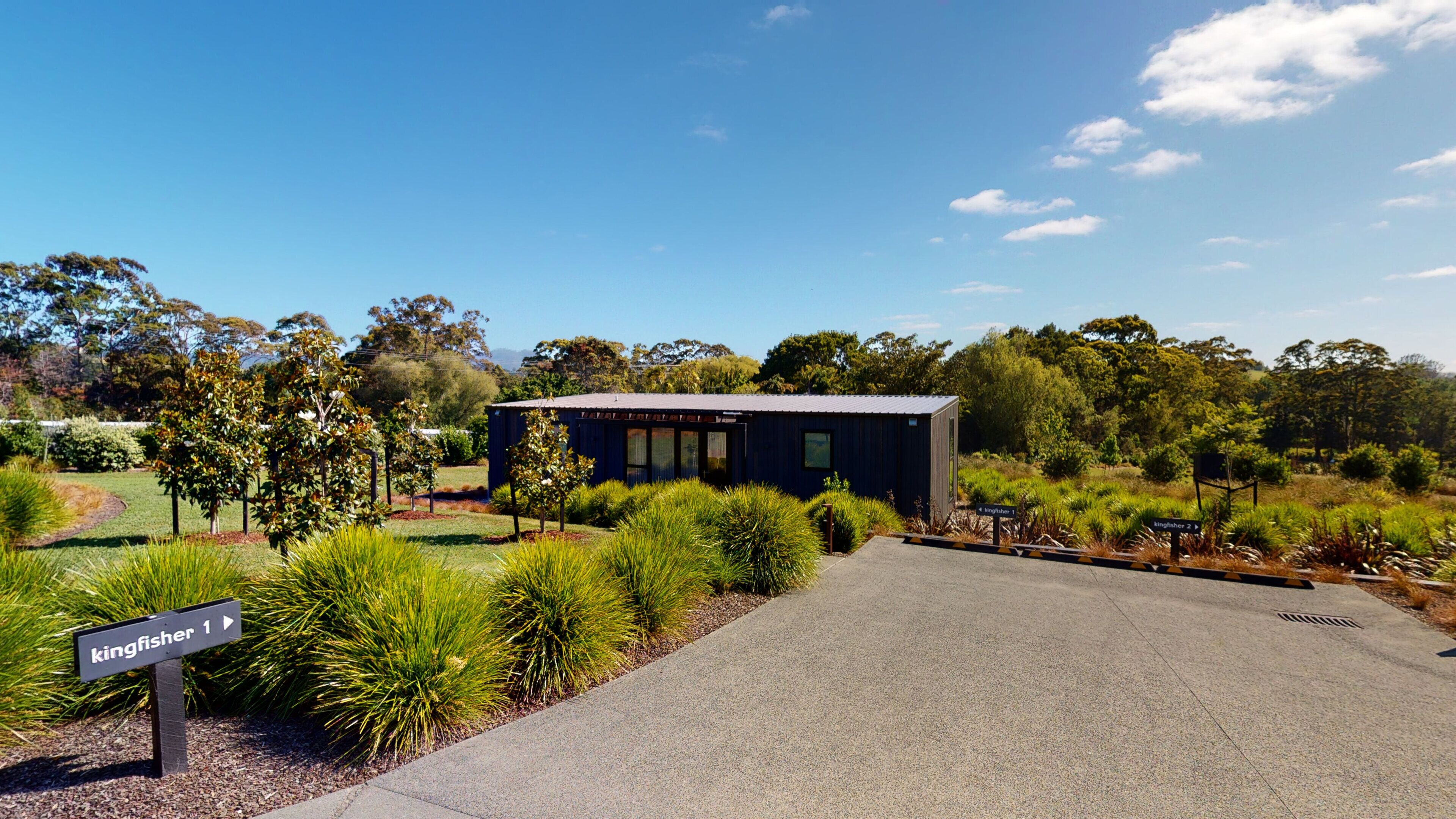 A modern building with a metal roof, surrounded by well-maintained gardens and trees.