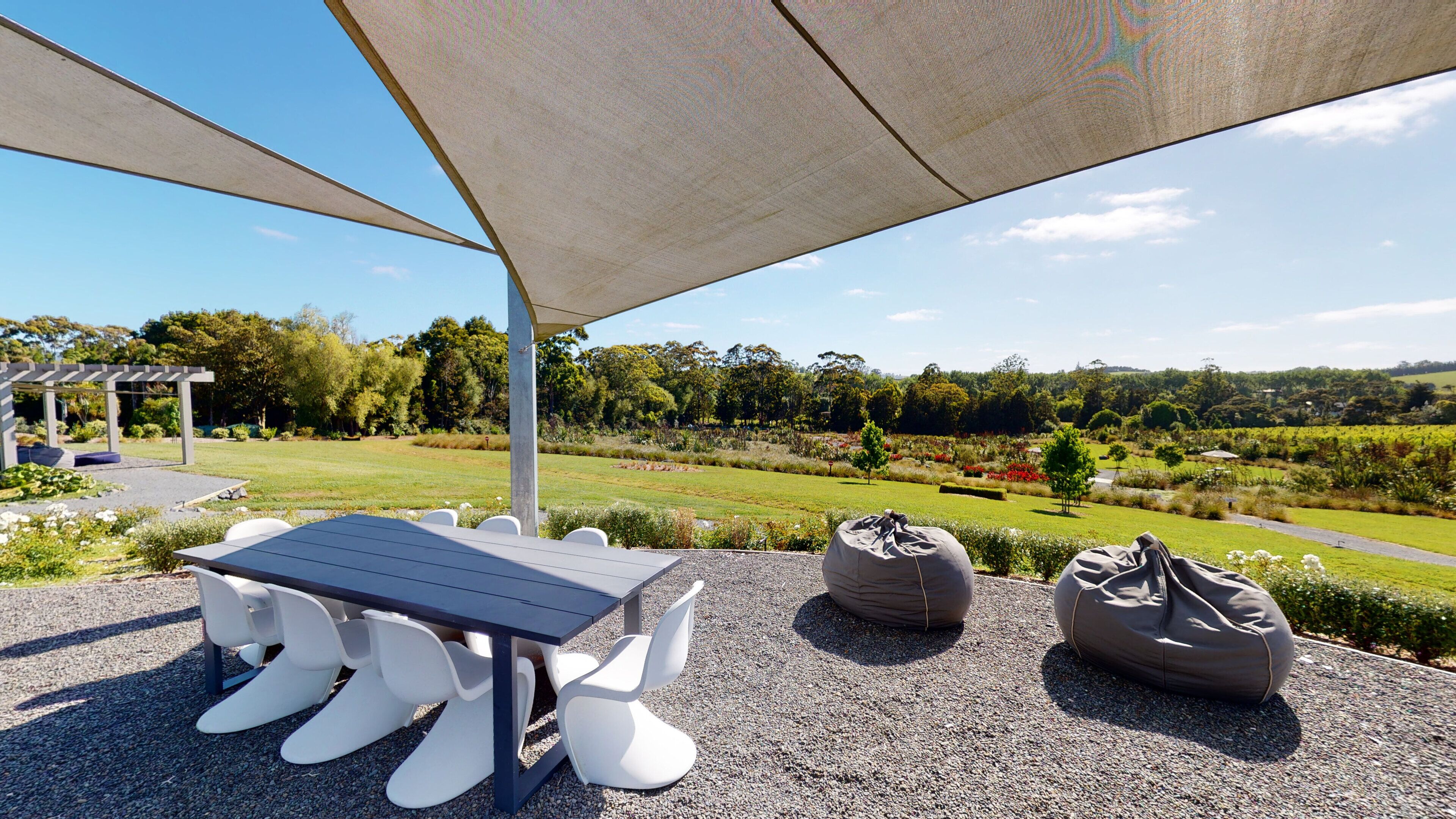 Een terras buiten met een tafel, stoelen, een pergola en uitzicht op een aangelegde tuin.