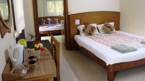 A bedroom with a wooden bed, a bedside table with a kettle, a vase with flowers, and a chair. - Mama Mids Home (Morjim)