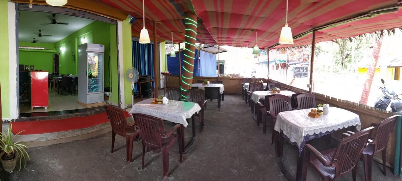 Ein Restaurant im Freien mit Tischen, Stühlen, einem Kühlschrank und einem Ventilator.