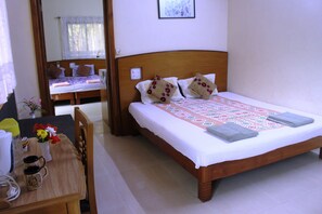 A neatly made bed with a patterned bedspread and pillows, a wooden nightstand with a vase of flowers, and a chair. - Mama Mids Home (Morjim)