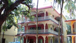 A multi-story building with balconies and arched doorways, surrounded by trees. - Mama Mids Home (Morjim)