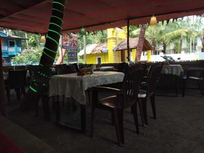 An outdoor dining area with tables and chairs, some with green lighting. - Mama Mids Home (Morjim)