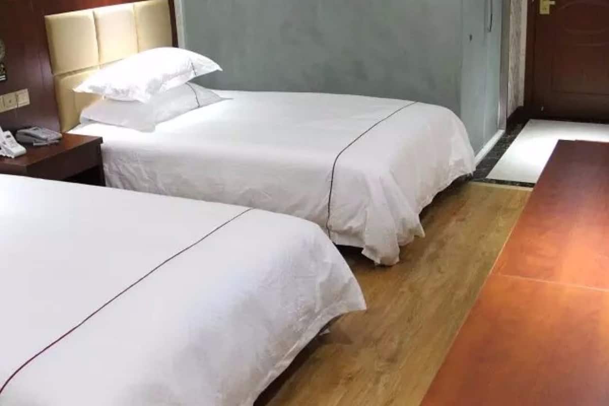 A hotel room with two single beds, a wooden floor, a nightstand with a phone, and a door to the right.