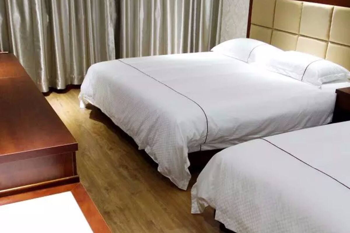 A hotel room with two beds, a wooden nightstand, and a large window with curtains.